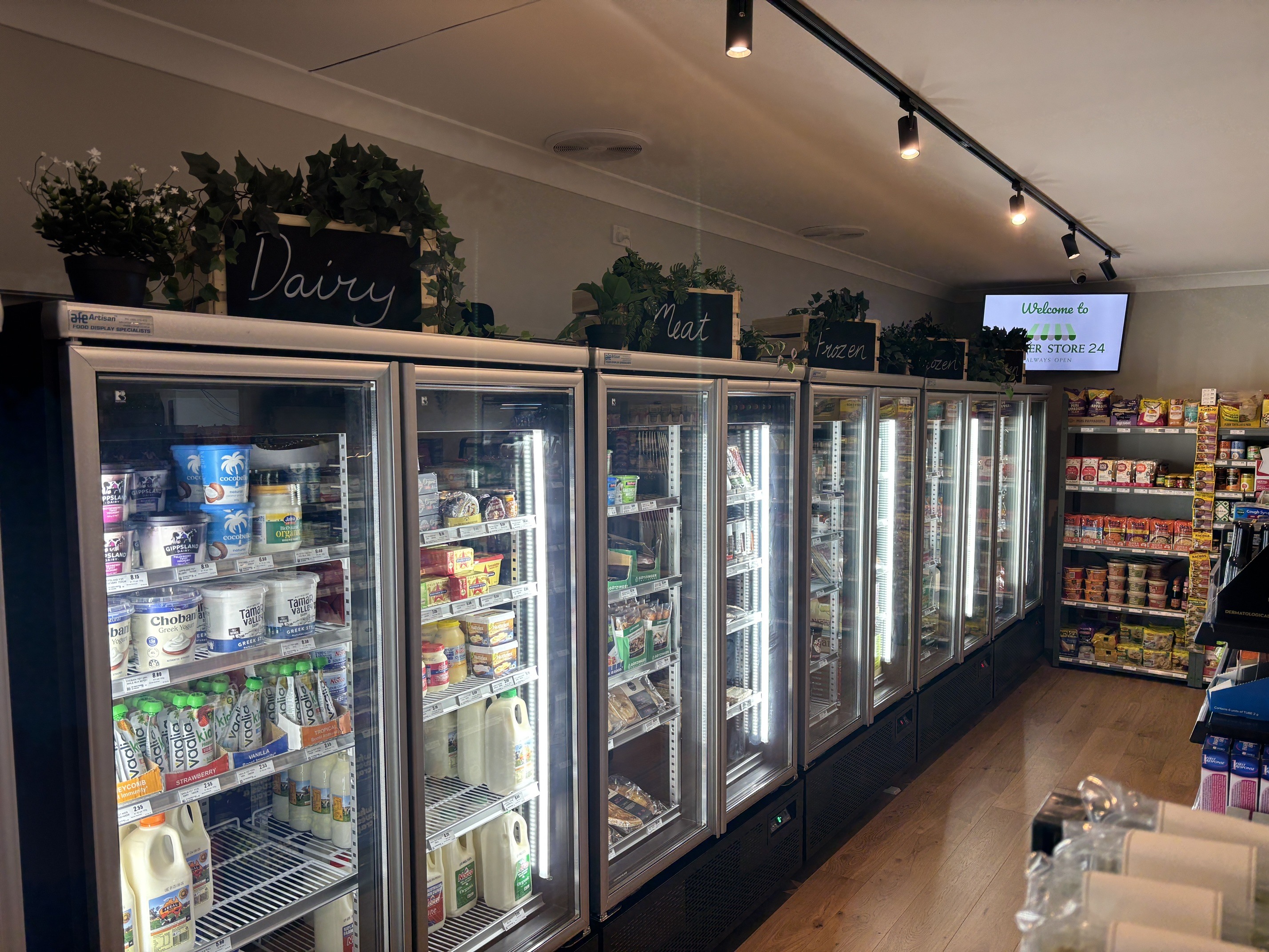 A line of glass-door refrigerators labelled Dairy, Meat and Frozen inside Corner Store 24