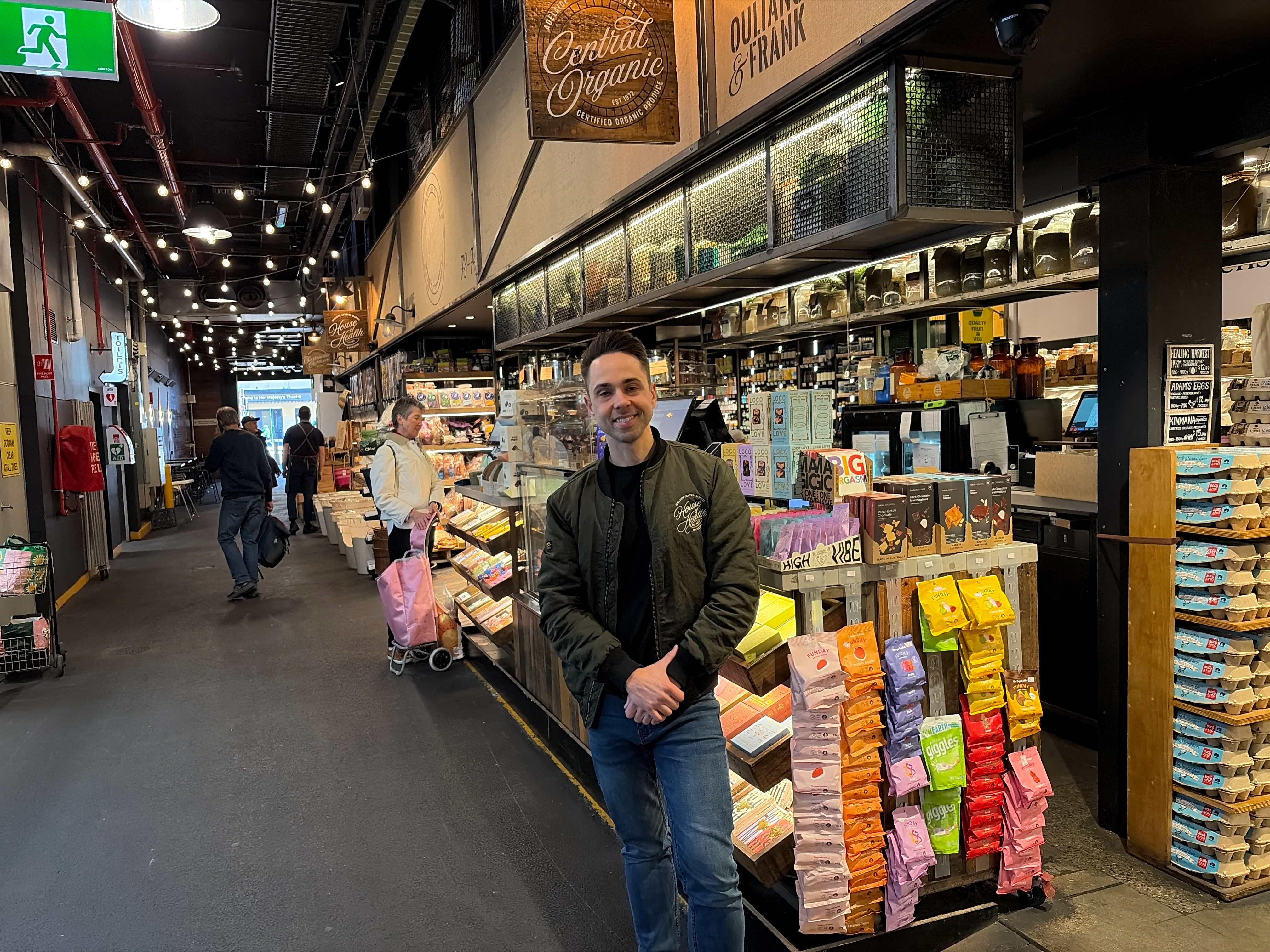 House of Health Collective store owner smiling in the Central Market store aisle beside the produce and grocery displays